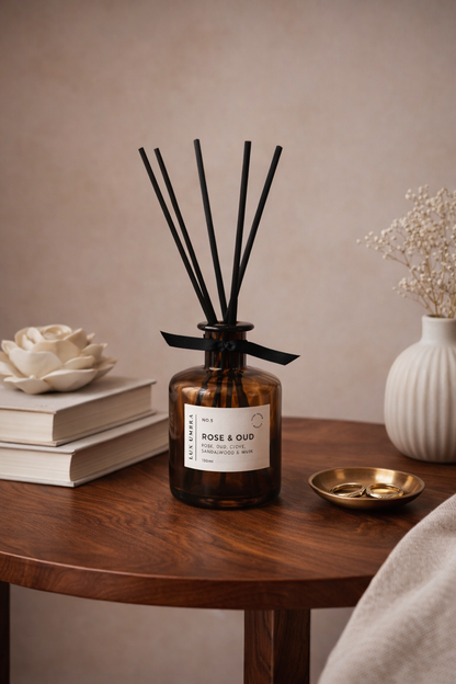 Rose and Oud scented Diffuser bottle with black sticks on a wooden table with decorative items.