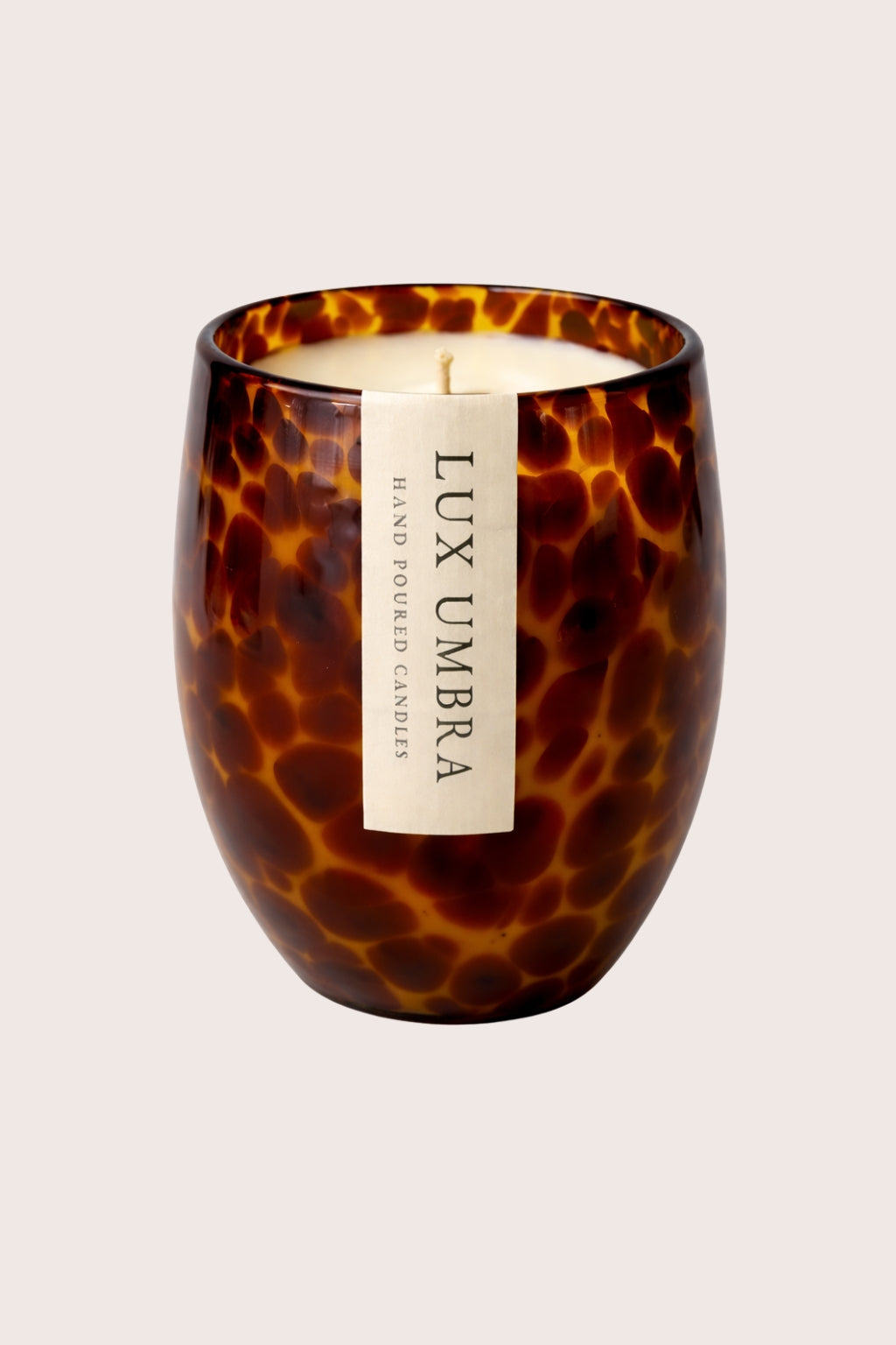 Candle in a tortoiseshell-patterned container with 'Lux Umbra' label on a light background