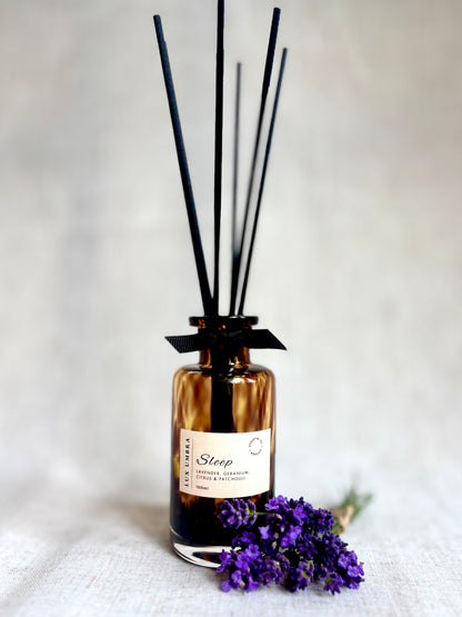 A brown tortoiseshell diffuser with black sticks and a label, accompanied by purple flowers on a light background 