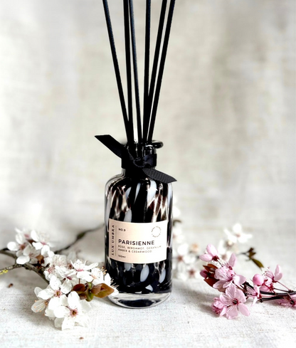 A black tortoiseshell patterned reed diffuser surrounded by blossom.