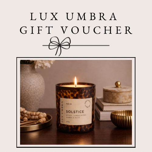 Candle with 'Lux Umbra' branding on a decorative table setting, featuring a gift voucher text overlay.