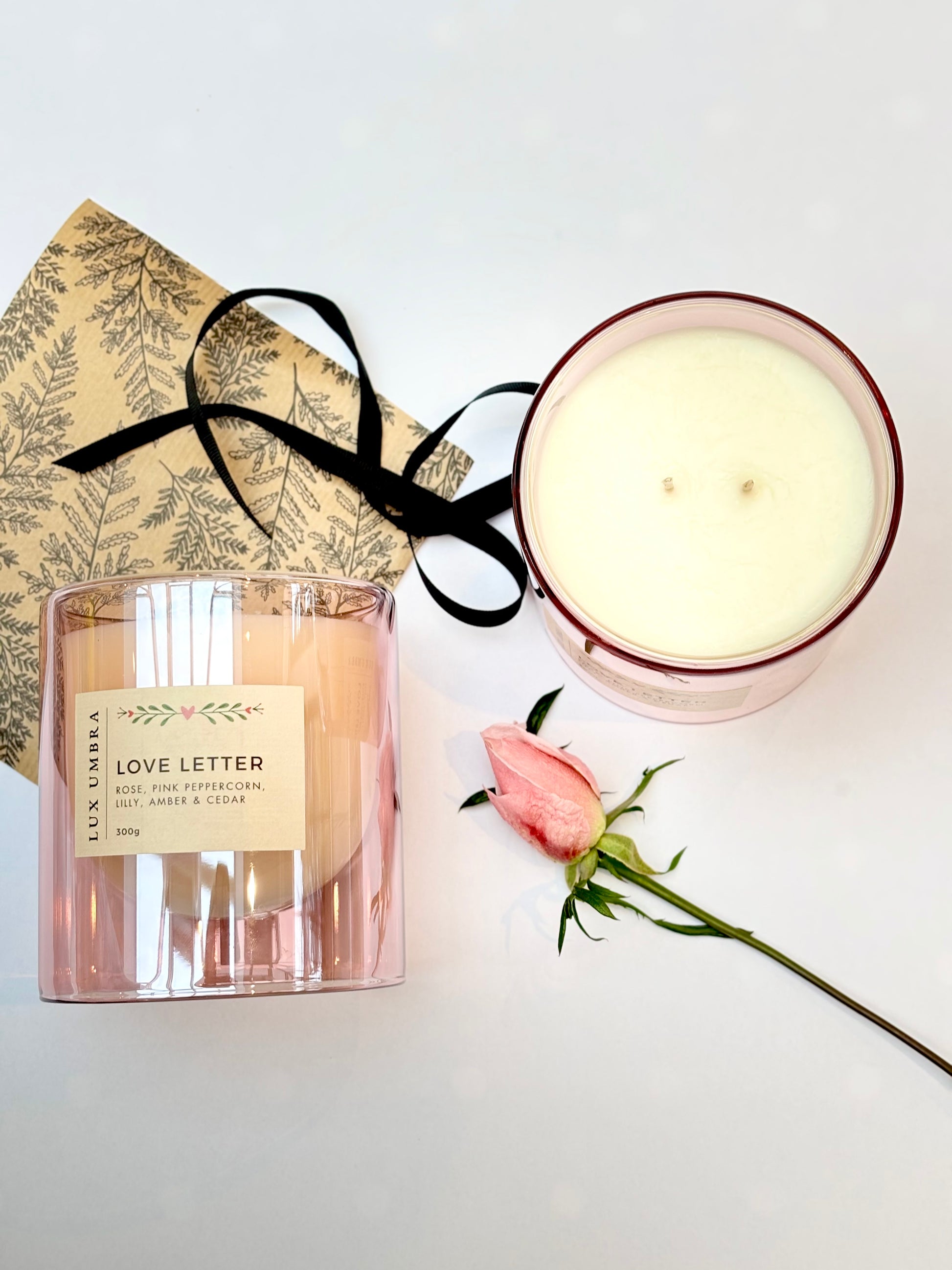 A flatlay photo of a double wicked candle called love letter. It also show pretty wrapping paper and black ribbon