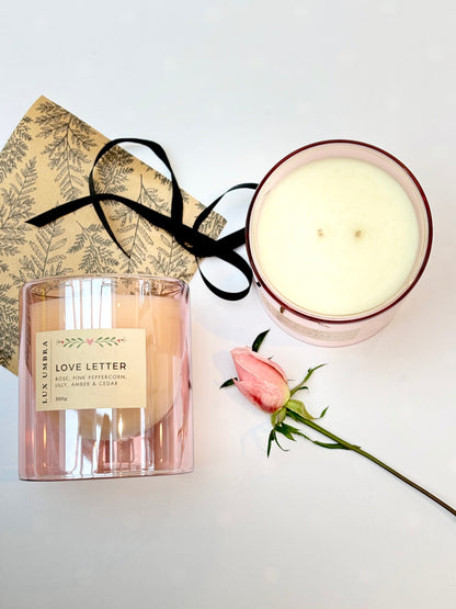 A flatlay photo of a double wicked candle called love letter. It also show pretty wrapping paper and black ribbon