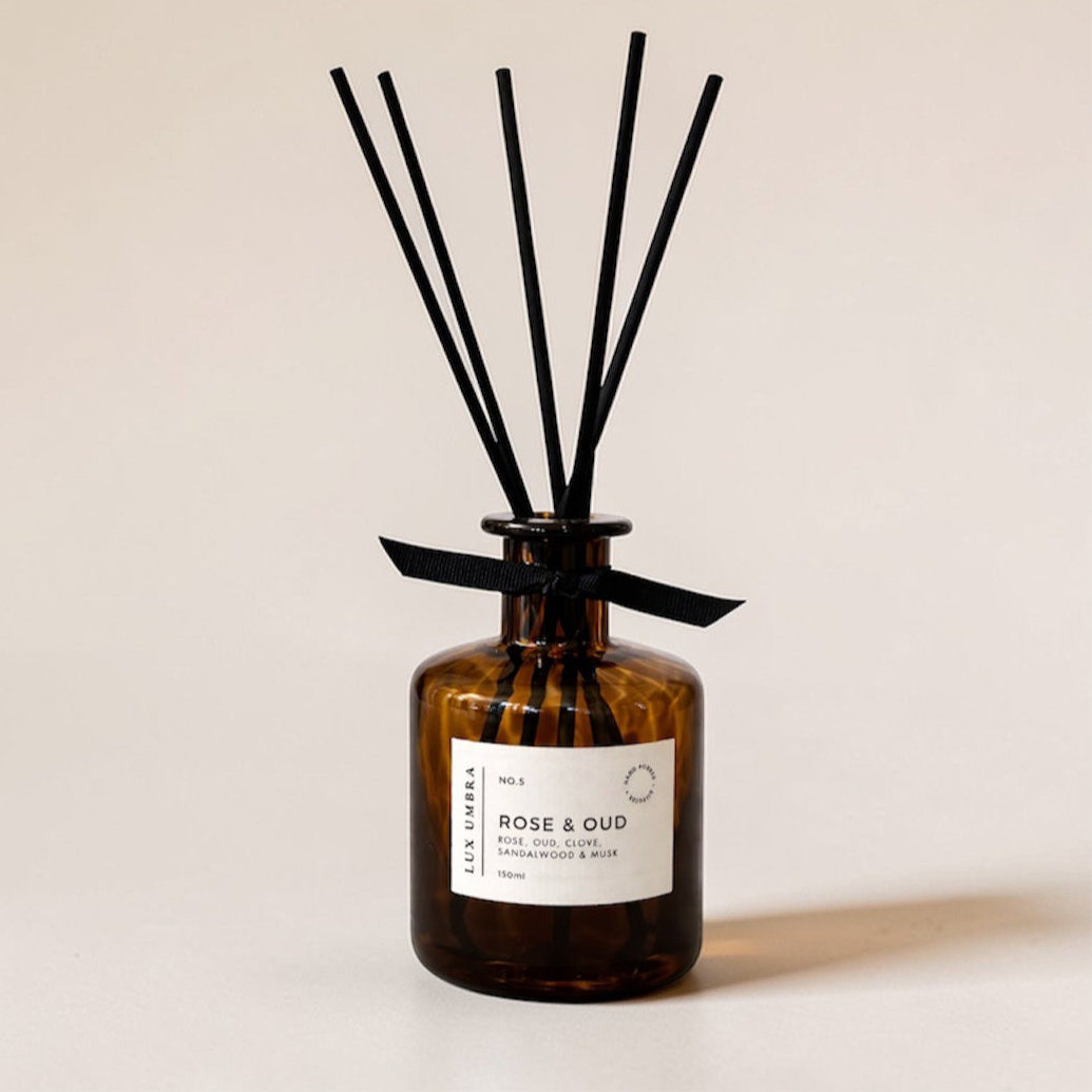 Brown diffuser bottle with a Rose and Oud scent with black sticks on a beige background