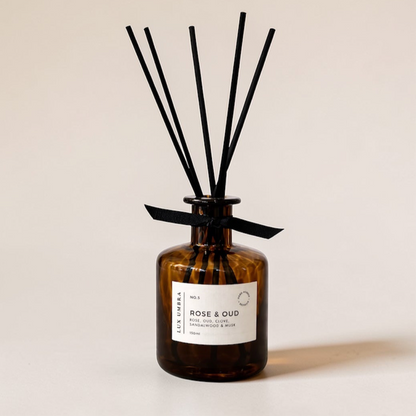Brown diffuser bottle with a Rose and Oud scent with black sticks on a beige background