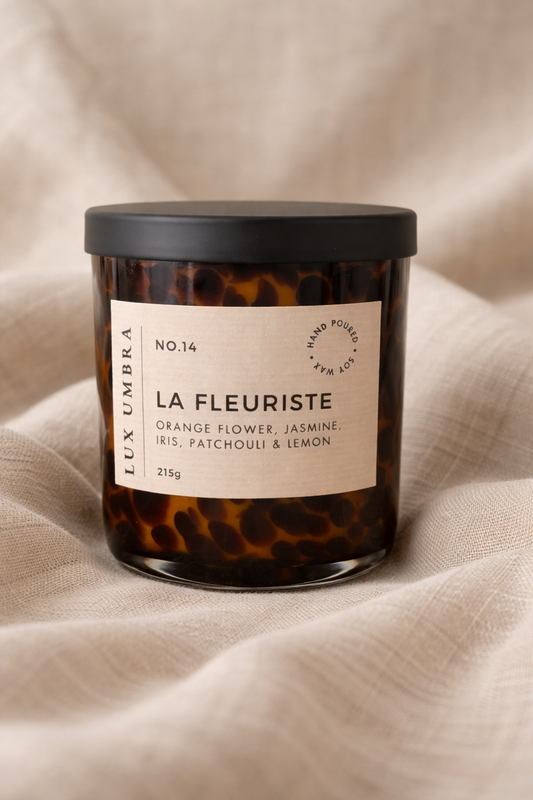 Candle with tortoiseshell pattern and 'La Fleuriste' label on a beige fabric background