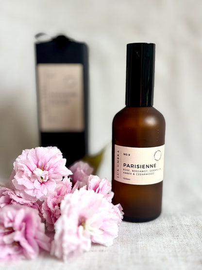 Parisienne room spray in an amber bottle next to cherry blossom. 