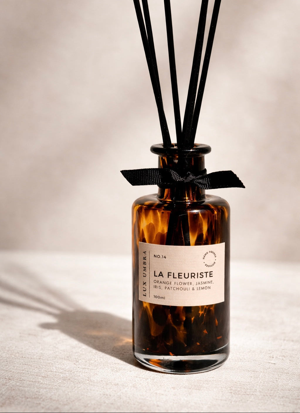 A tortoiseshell-patterned diffuser bottle with black reeds on a neutral background
