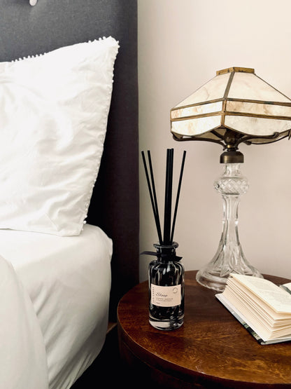 A black tortoiseshell diffuser on a bedside table next to a bed with white pillows.