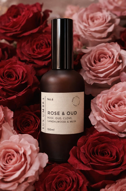 Bottle of Rose & Oud room spray surrounded by red and pink roses