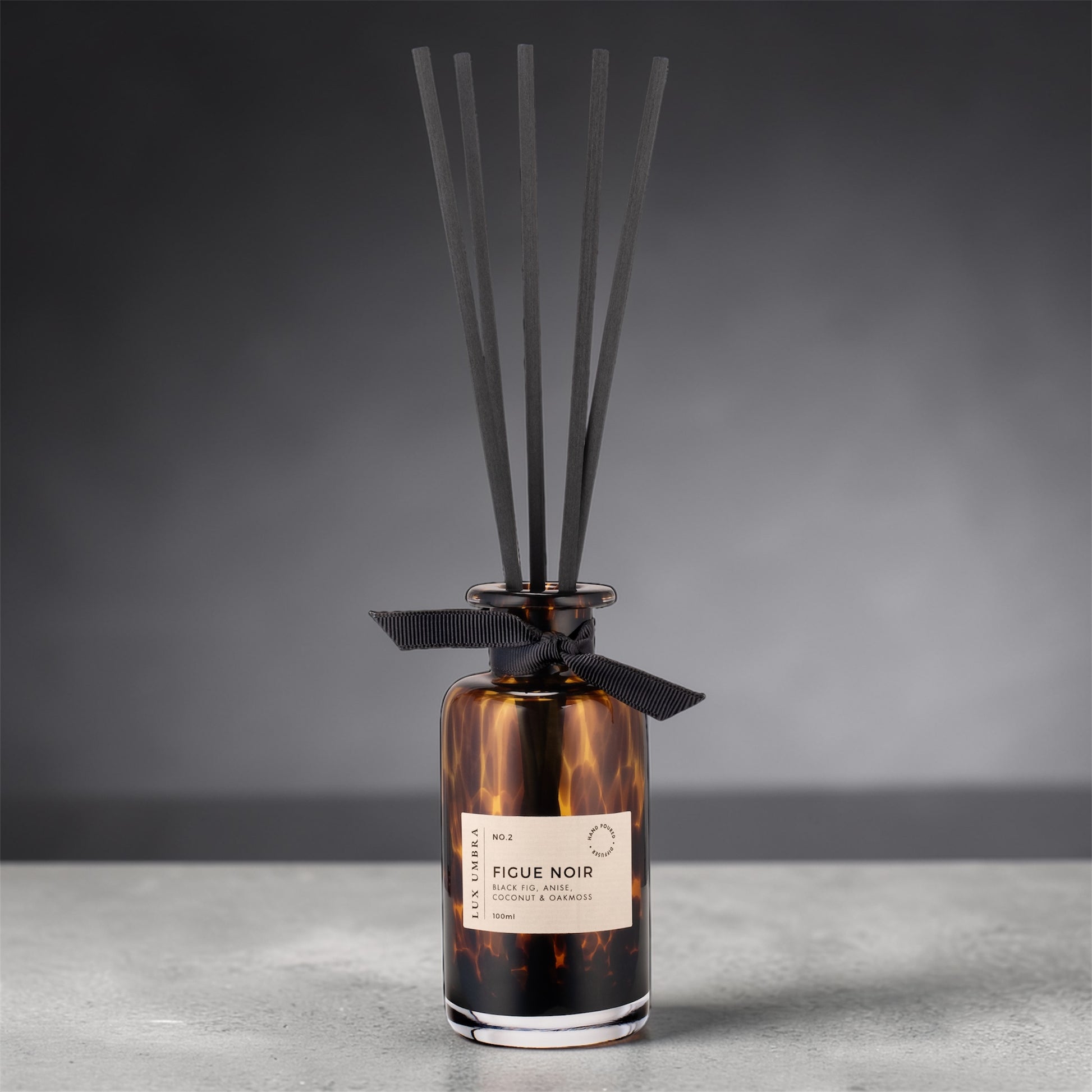 Reed diffuser with tortoiseshell design and black ribbon on a gray background