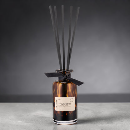 Reed diffuser with tortoiseshell design and black ribbon on a gray background