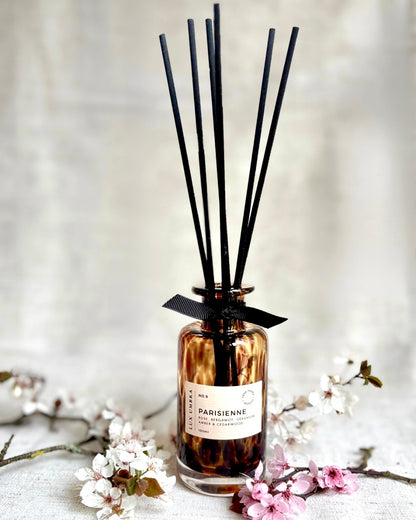 A brown tortoiseshell patterned reed diffuser surrounded by blossom 