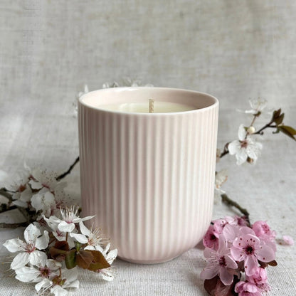 Pink ribbed ceramic candle jar, surrounded by cherry blossom. 