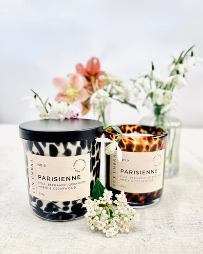A black tortoiseshell and brown tortoiseshell candle, called Parisienne, on a table with jars of spring flowers. 