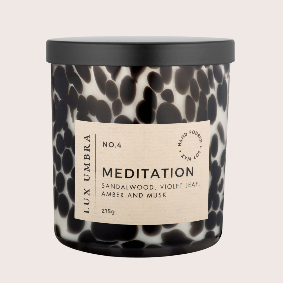 A luxury scented candle named 'Meditation' in a black and white tortoiseshell jar, with a black lid and a label displaying the fragrance notes.