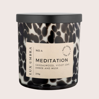 A luxury scented candle named 'Meditation' in a black and white tortoiseshell jar, with a black lid and a label displaying the fragrance notes.