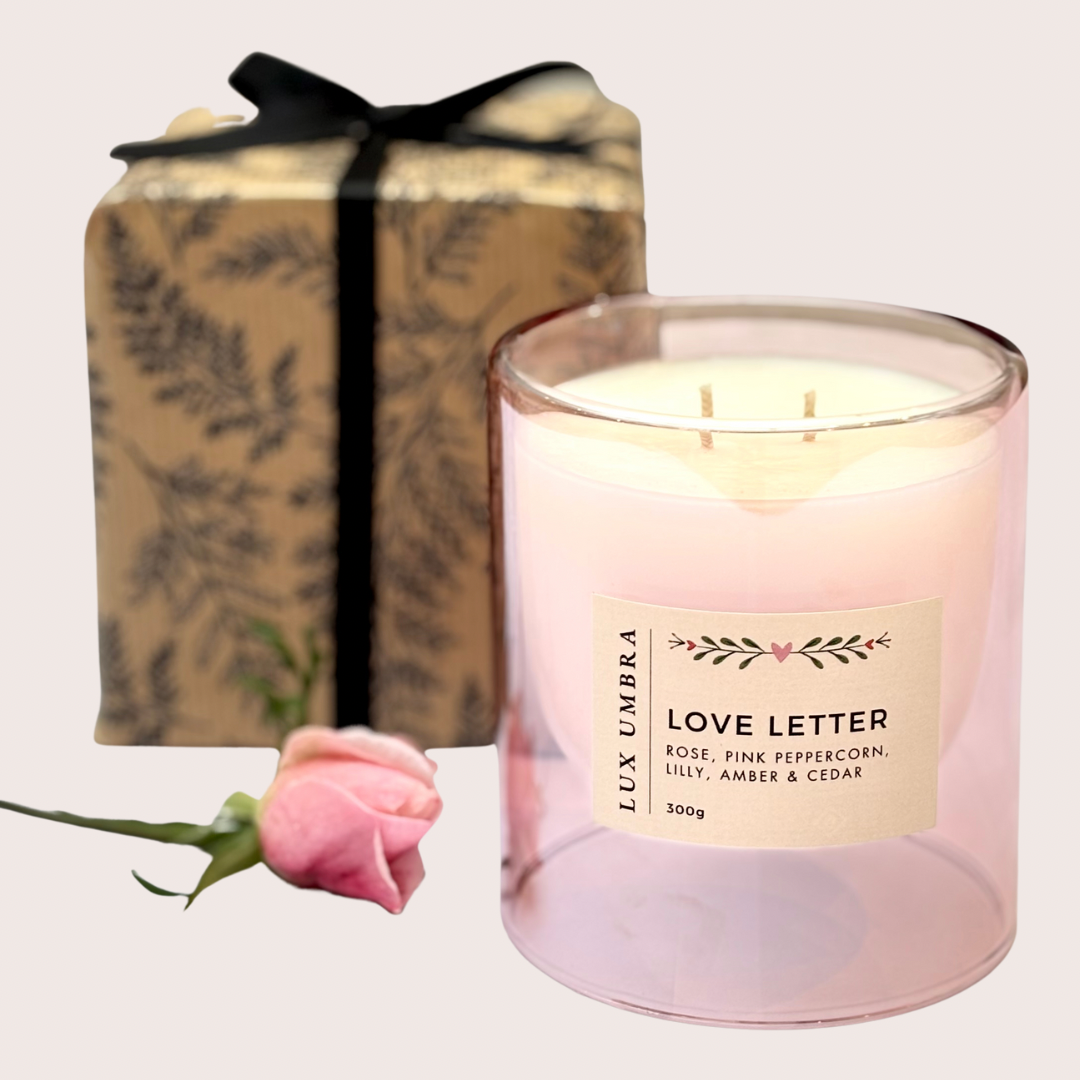 A pink double wicked candle called love letter. In the background is a candle wrapped in pretty paper and black ribbon