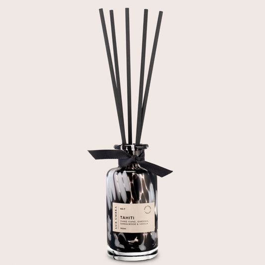 A black reed diffuser with a tortoiseshell patterned glass jar, six black fibre reeds, and a label reading 'TAHITI'. On a beige background.