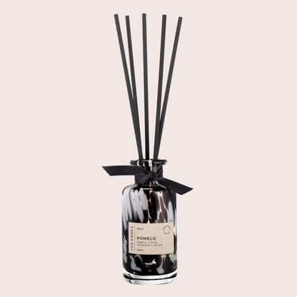 A black tortoiseshell diffuser with black Reed’s, adorned with a black ribbon. Set against a beige background