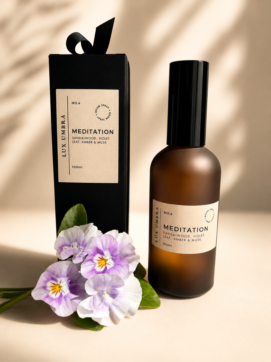 Lux Umbra Meditation room spray bottle and packaging with flowers on a neutral background